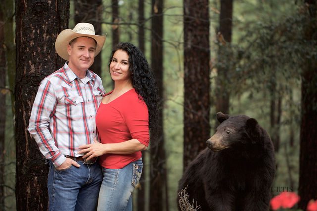 A man and woman posing for the camera in front of a bear.