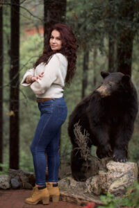 A woman standing next to a bear in the woods.